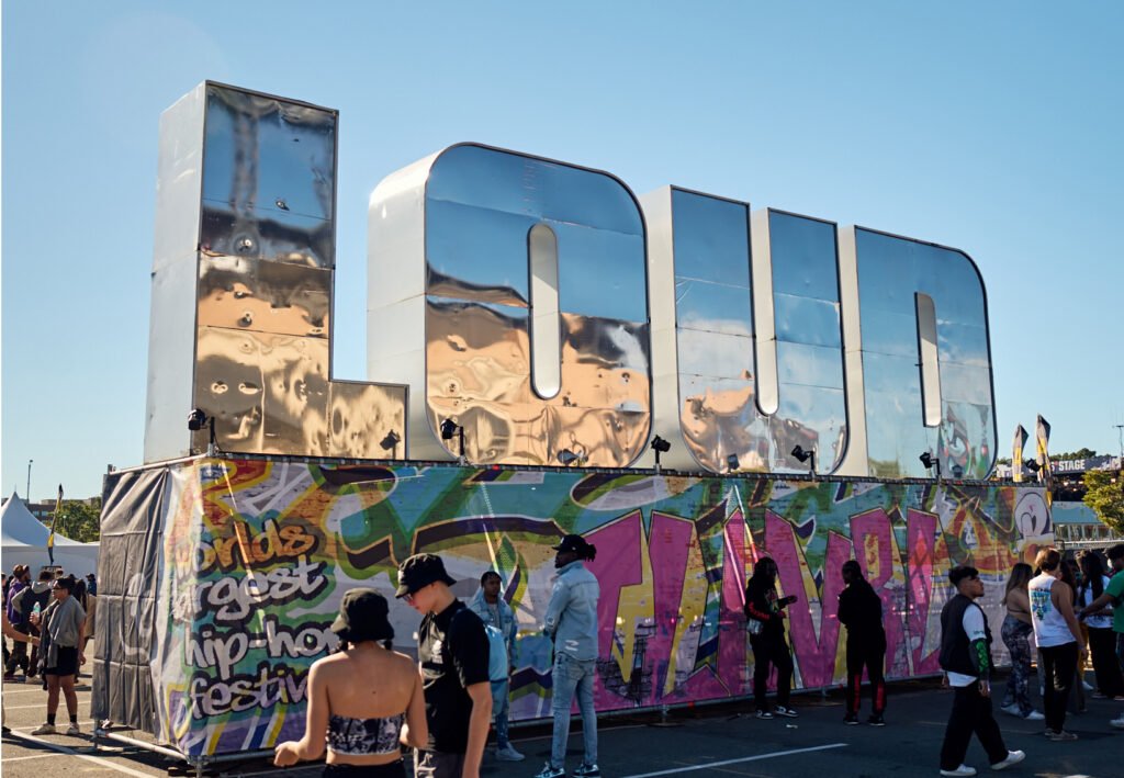 Festival crowd in front of a giant chrome "LOUD" sign and a graffiti-covered hip-hop festival wall