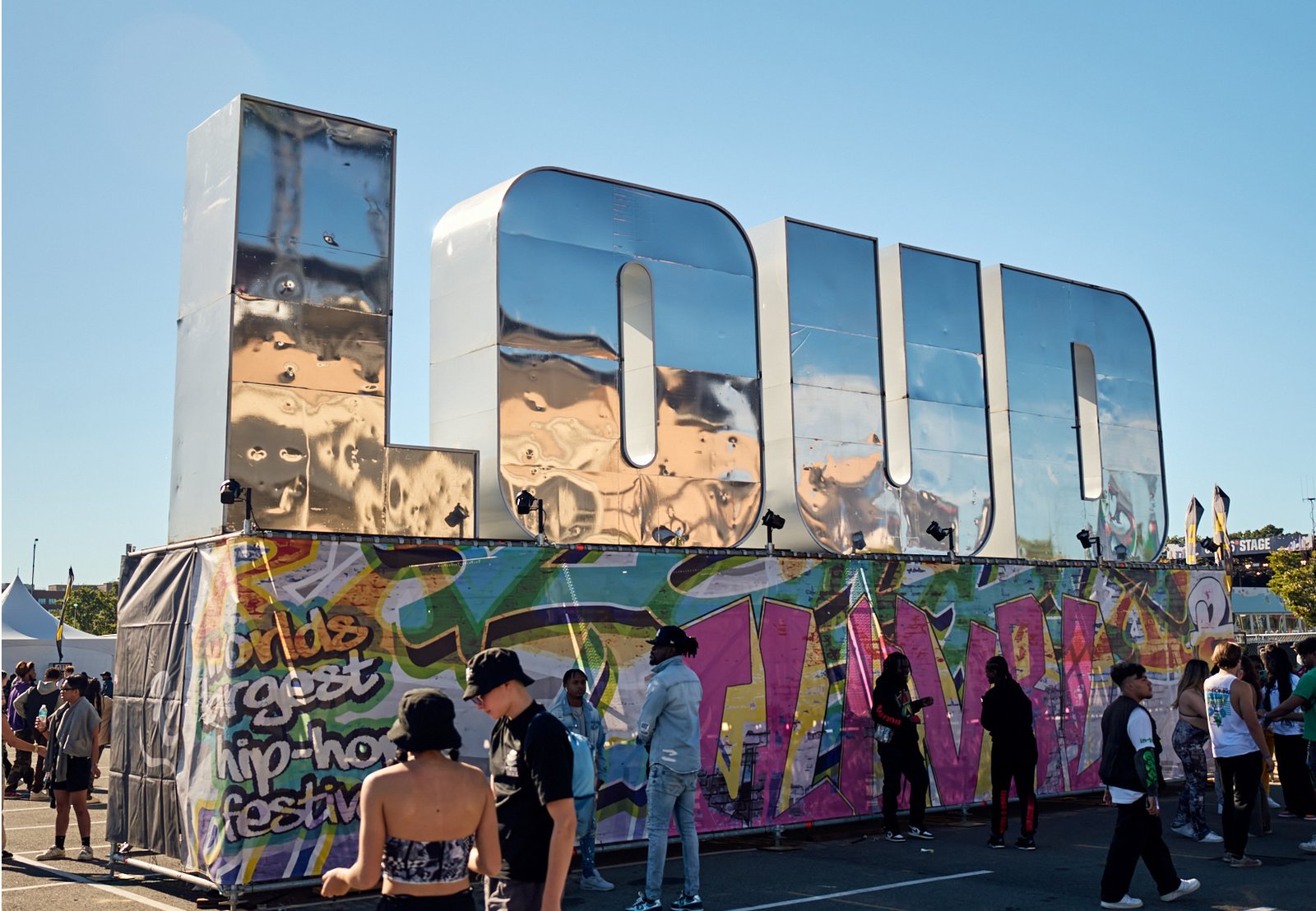 Festival crowd in front of a giant chrome "LOUD" sign and a graffiti-covered hip-hop festival wall